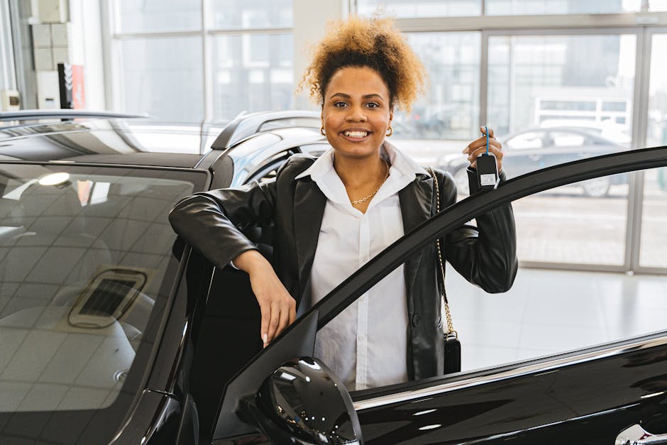 Smiling woman with car keys standing beside her new vehicle in a dealership showroom
