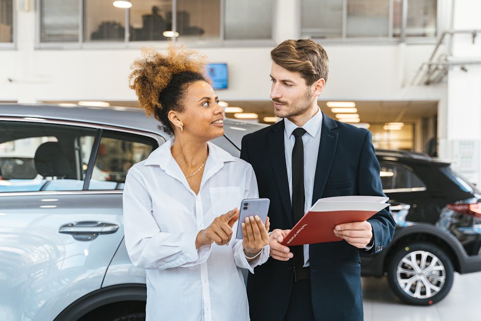African American woman and Caucasian man discuss car purchase at dealership using smartphone