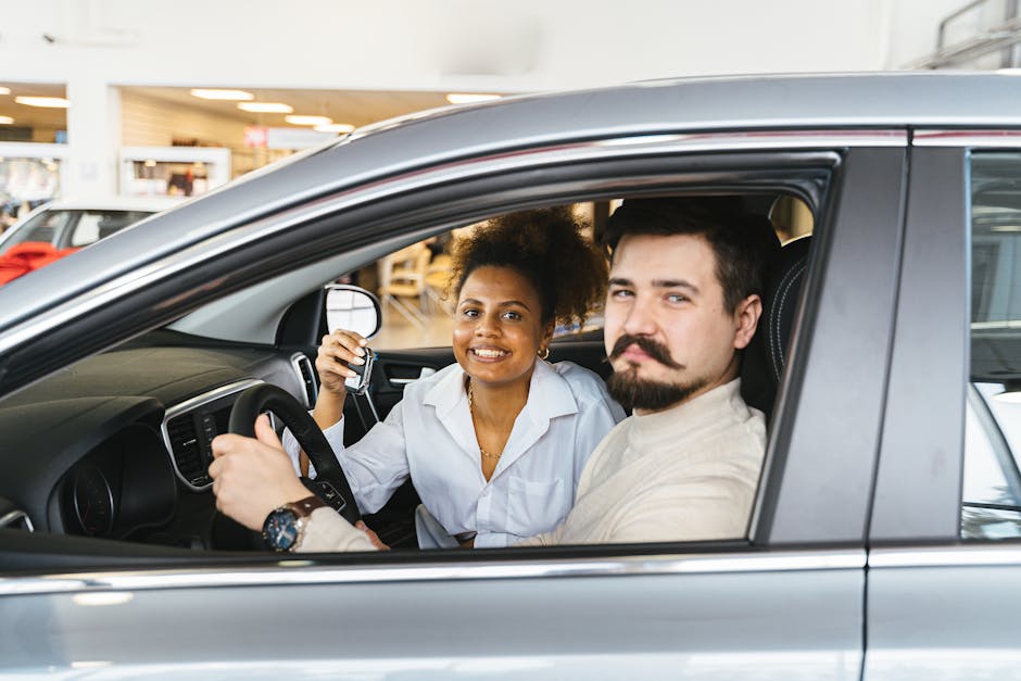 A smiling couple sitting inside a new car, holding the key and looking pleased